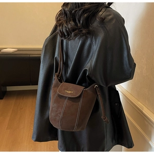 Detail of a brown suede bucket bag featuring contrast stitching and gold brand lettering