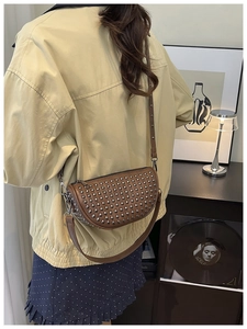 Detailed view of a brown punk-style crossbody bag with silver stud rivets worn by a model