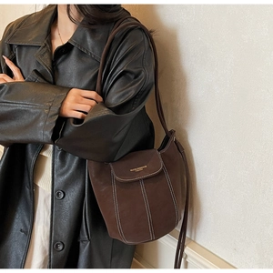 Detail of dark brown suede bucket bag with contrast stitching and golden logo stamp