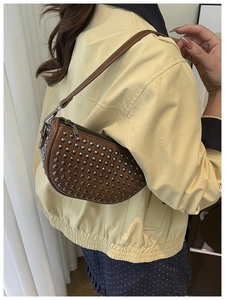 Close-up of brown crescent bag with silver stud details and shoulder strap on model
