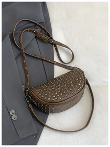 Close-up of brown half-moon crossbody bag with silver rivet studs on suit fabric
