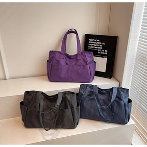Three multi-pocket canvas tote bags in purple, grey, and navy on a white display stand