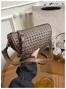 Detail of brown leather crossbody bag featuring silver metal studs and adjustable strap