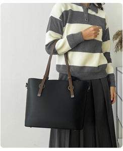 Détail d'un grand cabas en cuir grainé noir avec des lanières marron et boucles métal