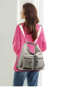 Close-up of light grey nylon backpack showing dual front zipper pockets and wide straps