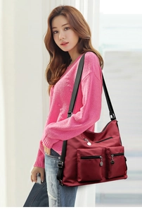 Close-up of a burgundy nylon crossbody bag with dual zipper pockets on a female model