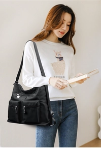 Close-up of black nylon shoulder bag featuring dual front zipper pockets on a female model