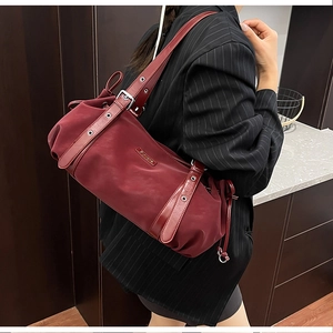 Bordeaux red cylindrical shoulder bag with silver grommets worn over the shoulder