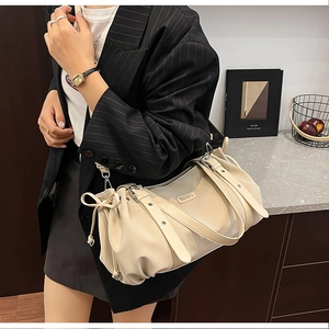 Detail of a creamy beige leather tote bag with a metal logo and side drawstring knots