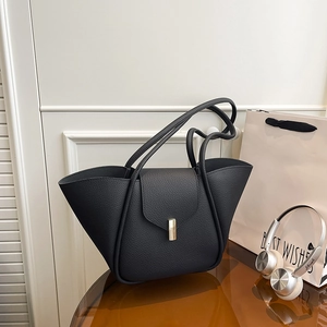 Elegant black lychee leather wing tote bag with gold metal buckle on a glass table