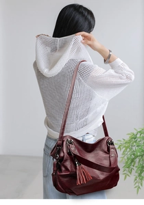 Detailed view of burgundy faux leather shoulder bag with chic fringe tassel and pebbled texture