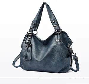 Close-up of matte blue leather tote bag showing side view with dual fringe tassel detail