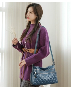 Detail of dark blue quilted crossbody bag with triple zippers and soft leather texture