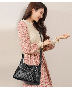 Detail of black quilted crossbody bag featuring three functional zip compartments and chain