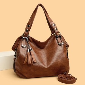 Brown faux leather tote bag with tassels and detachable strap in a minimalist setting
