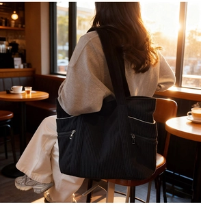 Detail of black corduroy tote bag showing multiple pockets and metallic zipper closure