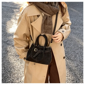 Detail of black bucket bag with white contrast stitching and gold metal buckle on shoulder strap