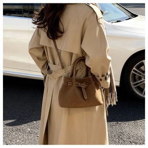 Brown leather bucket bag with white stitching and bow detail shown in outdoor street style
