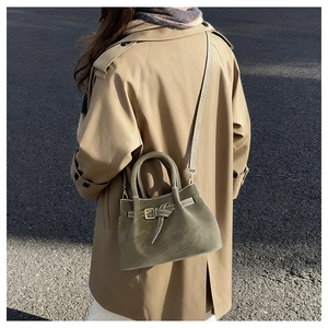 Detail of olive green suede bucket bag featuring decorative belt buckle and top handles