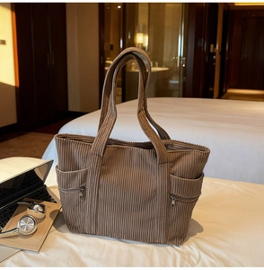 Detail of dark brown corduroy tote bag featuring side pockets on a cozy bed background
