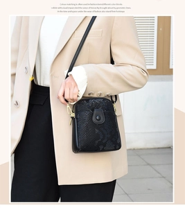 Street style shot of a black snakeskin pattern crossbody bag with gold metal hardware