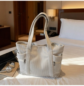 Detail view of corduroy tote bag with side zipper pockets on a white bed