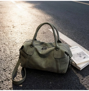 Detail of olive green suede Boston bag with textured leather and metal rivets in street light