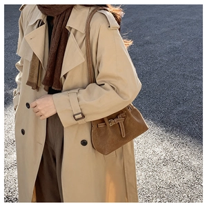 Close-up of brown suede bucket bag with leather strap buckle worn over a beige trench coat
