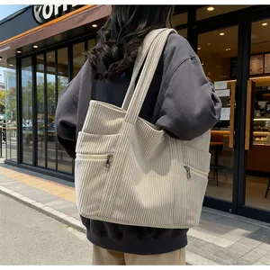 Close-up of beige corduroy tote bag featuring multiple pockets and metal zipper details