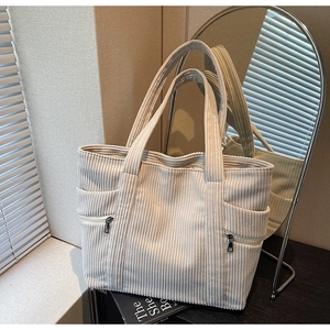 Detailed close-up of corduroy tote bag texture with functional side zipper and soft beige fabric