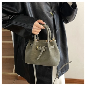 Detail of olive green bucket bag with golden belt buckle and sleek cylindrical handle