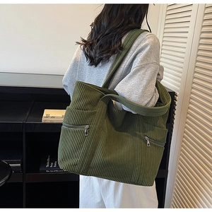 Detail of dark green corduroy tote bag featuring dual front zipper pockets and shoulder strap