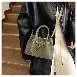 Olive green bucket bag with belt buckle detail shown on model against wooden stairs