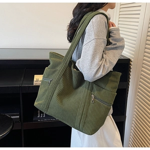 Close-up of olive green corduroy tote bag with dual front zipper pockets on model