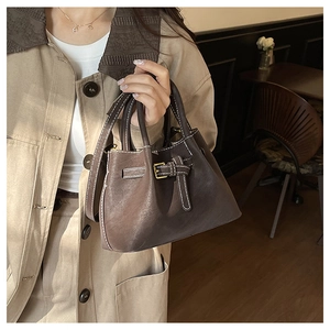 Close-up of dark brown bucket bag featuring white contrast stitching and buckle detail
