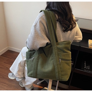 Detail view of dark green corduroy tote bag featuring multi-pocket design and wide straps