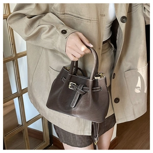 Detail of dark brown leather bucket bag with decorative strap and metal buckle