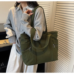 Detail of dark green corduroy tote bag showing side zipper pocket and ribbed texture