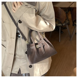 Detail of dark brown leather bucket bag with white stitching and metal buckle on trench coat