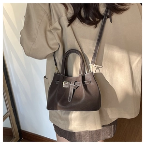 Detail view of brown bucket bag with white contrast stitching and metal buckle strap