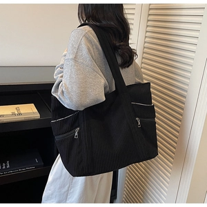Detail of a black corduroy tote bag featuring vertical texture and a side zipper pocket