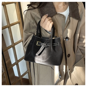 Detail of black leather bucket bag with white contrast stitching and gold buckle