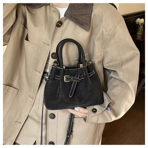 Detail of black bucket bag featuring white contrast stitching and decorative belt buckle