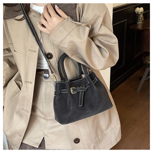 Detail of black leather bucket bag with white contrast stitching and metal buckle strap