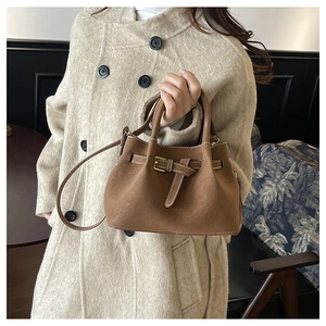 Brown bucket bag detail featuring white contrast stitching and decorative belt buckle