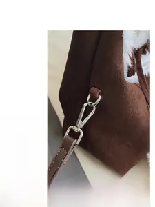 Détail du sac seau en daim marron foncé avec bordure en peluche blanche et boucles argentées