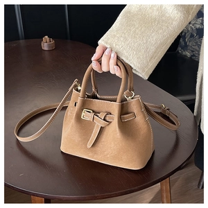 Close-up of tan leather bucket bag with contrast stitching and decorative belt buckle