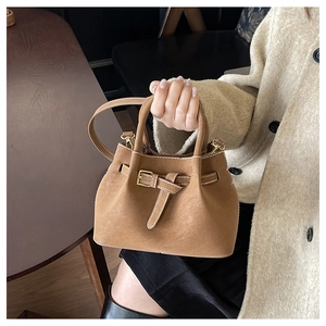 Detail of camel bucket bag showing matte texture and golden buckle in lifestyle setting