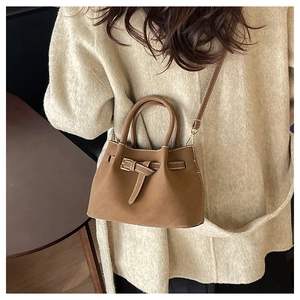 Detail of caramel brown bucket bag with gold hardware and leather strap on a person