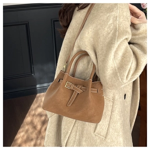 Brown bucket bag detail showing the metal buckle and long strap worn over a wool coat